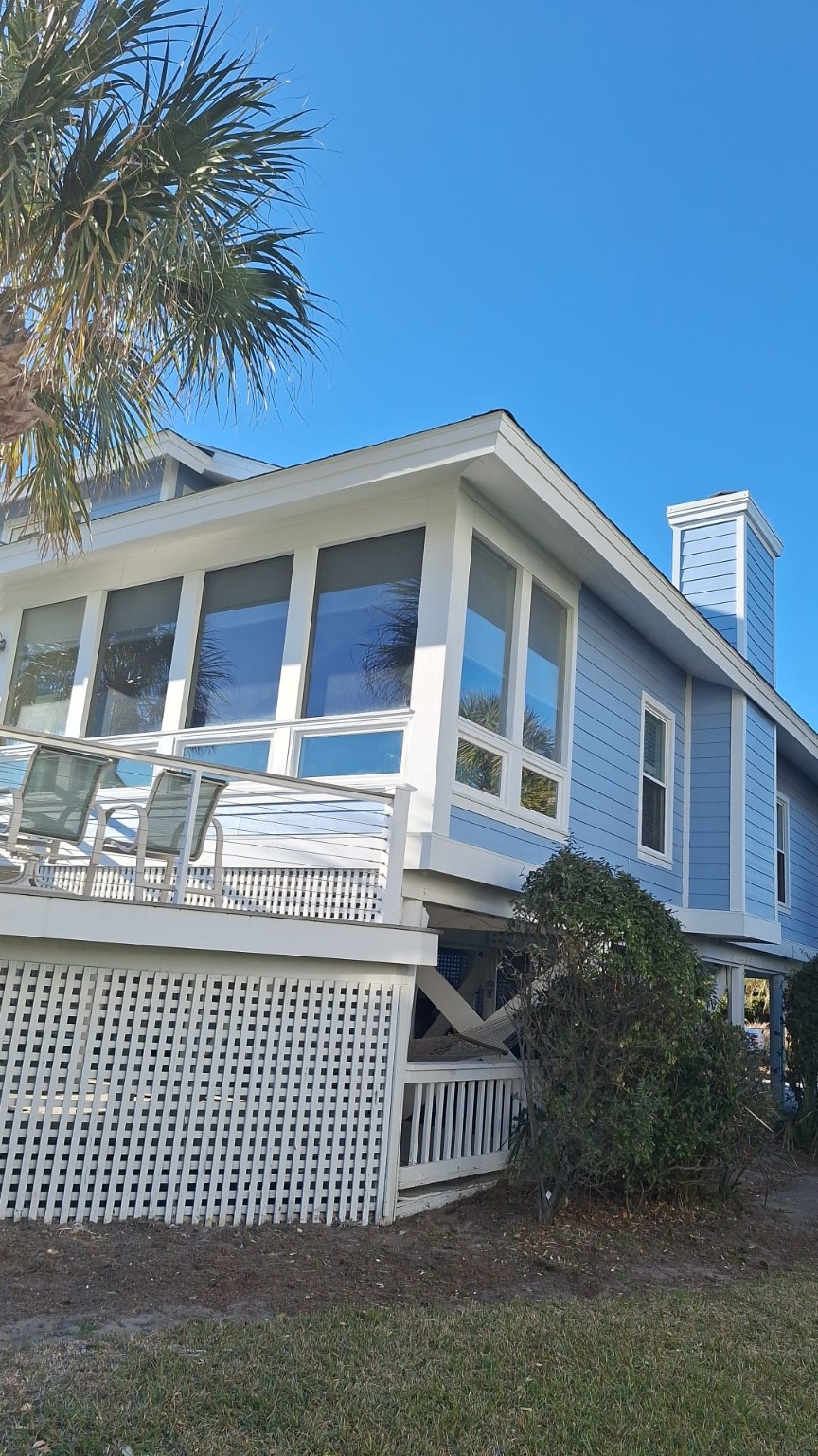 Porch corner of the blue coastal house showing white window trim, roofline and siding